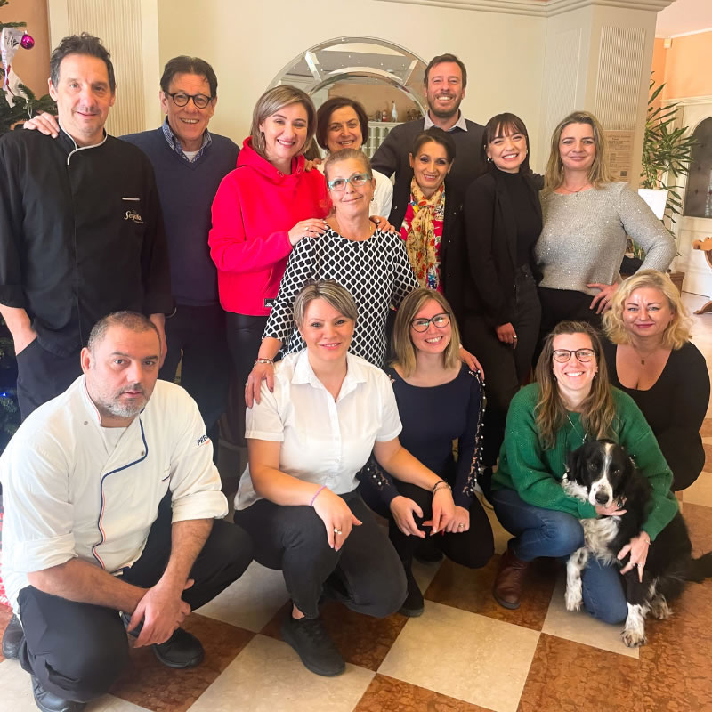 Gruppo di persone sorridenti con un cane in un interno accogliente.